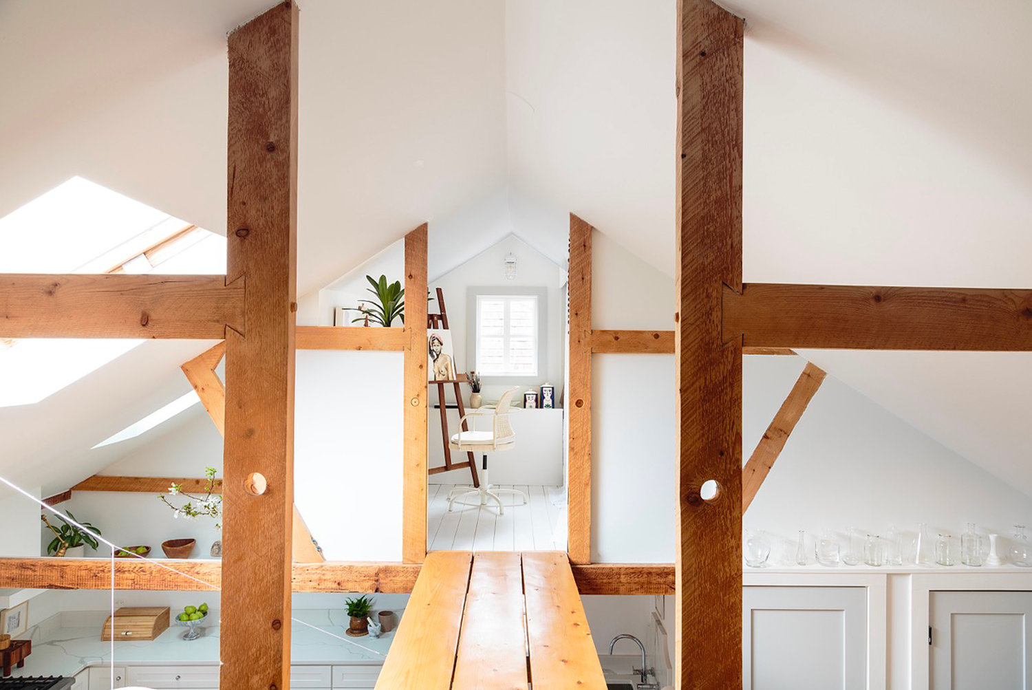High above the main living areas, the couple set up two small rooms where they can pursue work and hobbies. White walls bounce the light harnessed by several skylights. Wood beams add definition and warmth.