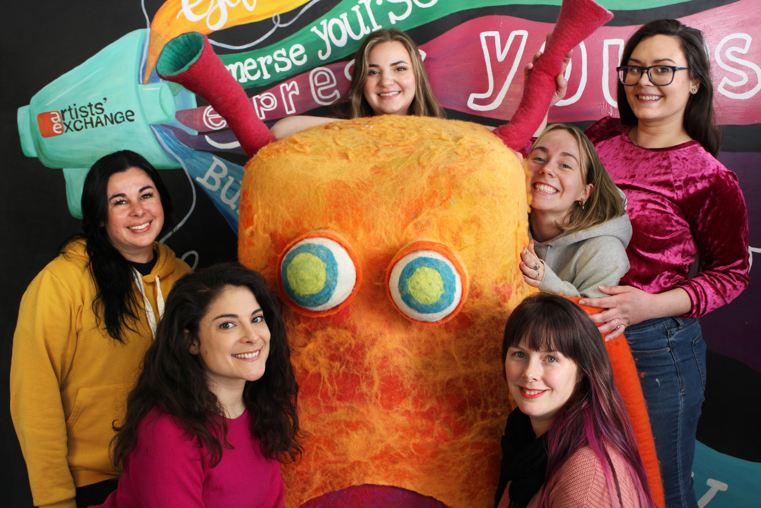 Artists' Exchange ladies with the mascot Woolly Nilly. Front Row: Vanessa Rundlett, Instructor; Shannon Casey, Director. Back Row: Jenny Sivo, Operations Manager; Abby Doyle, Assistant Teacher; Juliette Hoernle, Instructor; Emily Urban, Graphic Design