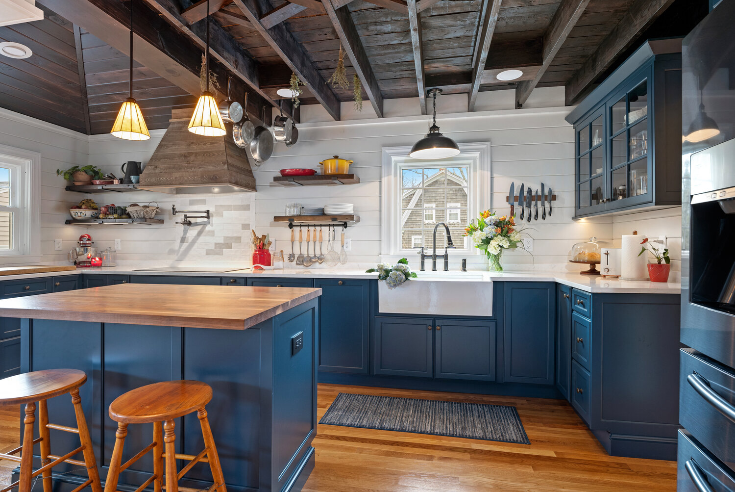 The wood in the floor, ceiling, range hood, and island adds warmth and contrast with the cool colors of the countertop, shiplap, cabinetry, and appliances